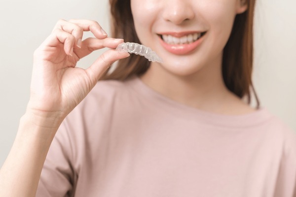 A woman holding her aligner, discovering the difference between it and metal or ceramic braces, getting her questions: “How does invisalign work?”, "Is Invisalign worth it?”, and “Does Invisalign hurt?” answered.