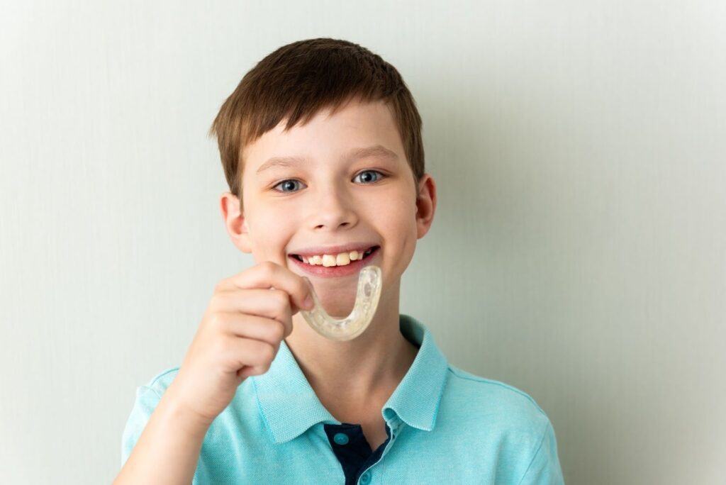 A teen holding his Invisalign Teen braces for kids, smiling confidently.
