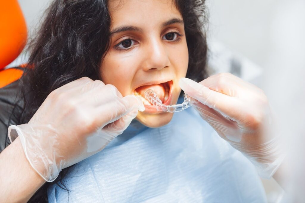 Dentist fitting Invisalign Teen braces for kids on a young girl's teeth.
