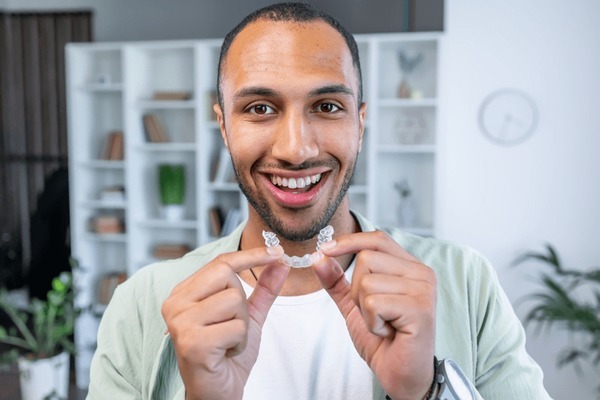 Man holding an Invisalign clear aligner and smiling because he came in with all of his questions to ask at his Invisalign consultation.