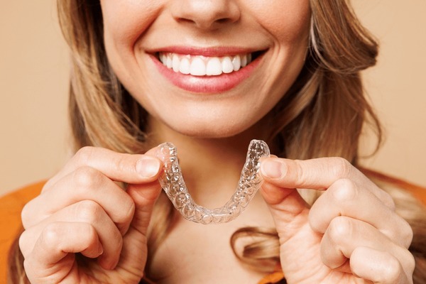 Woman smiling and holding a clear Invisalign aligner.