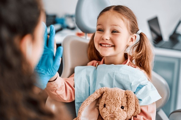 Smiling child holding a stuffed toy giving a high-five to the dentist during a BPA free pediatric dental filling visit.
