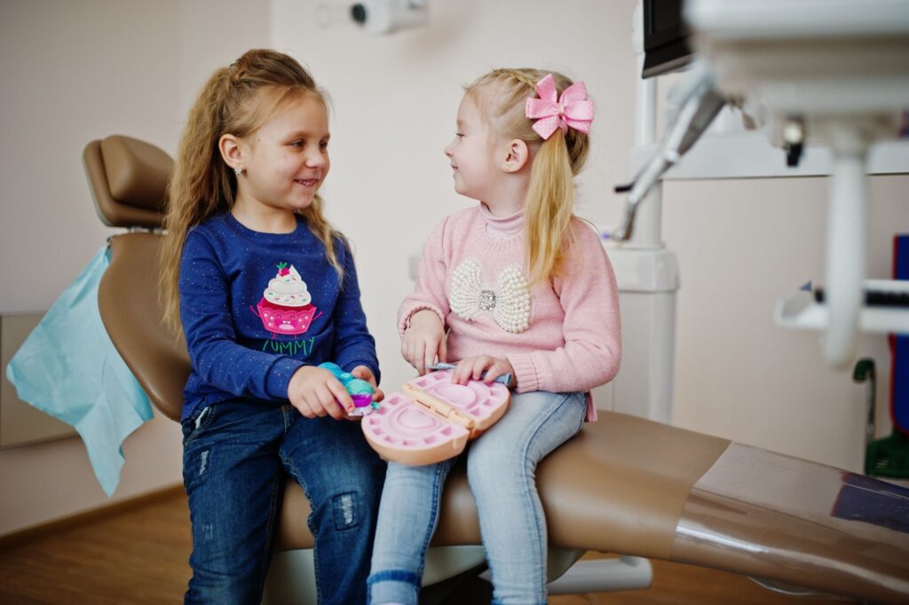 Two children sitting in a dental office holding a dental model during a BPA free composite tooth filling visit.