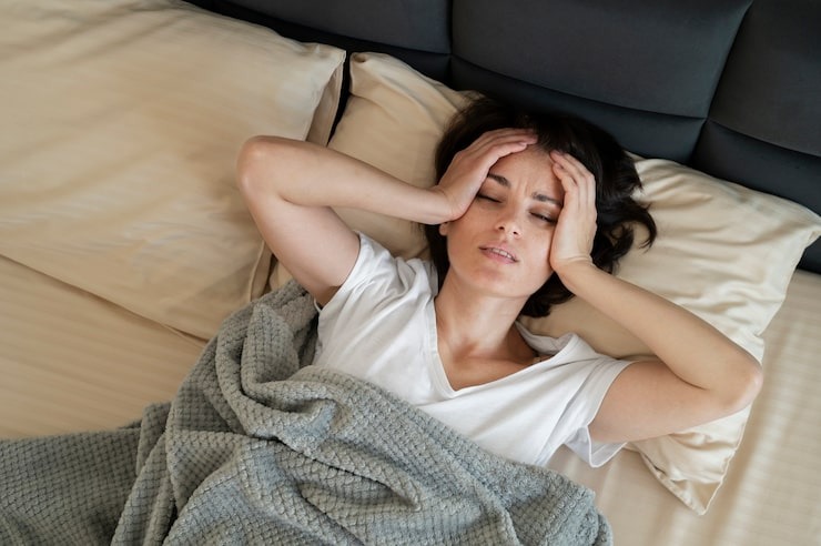 Tired woman in bed holding her head, showing obstructive sleep apnea symptoms, wonders: “Can sleep apnea kill you?” and needs sleep apnea treatment. With signs of sleep apnea, she needs an obstructive sleep apnea test.
