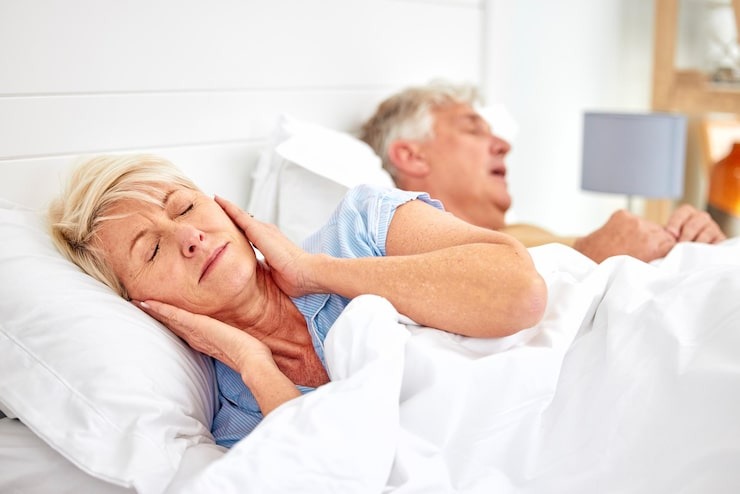 Woman struggling to sleep as her partner snores, illustrating sleep apnea symptoms.