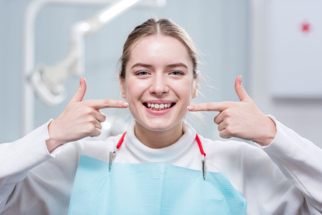 Smiling patient pointing at her tooth bridge after a bridge dental treatment, happy with her dental bridge cost.