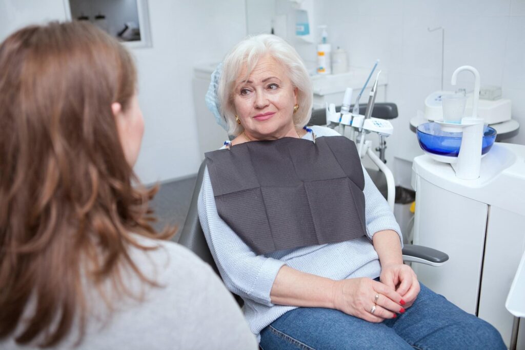 Patient sitting in dental chair, talking with dentist before a bone graft dental procedure.