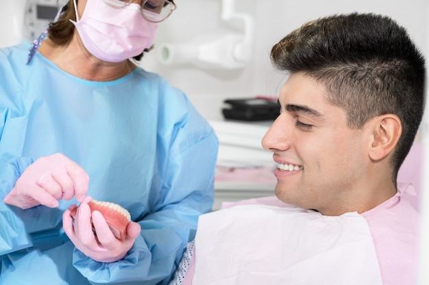 Dentist for implants near you showing an implant tooth model to a smiling patient, explaining implant tooth replacement options and implant tooth care.