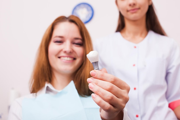 Smiling patient holding an implant tooth replacement with a dentist for implants near you.