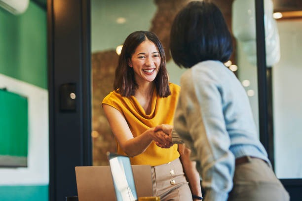 Two women smiling and shaking hands, showcasing increased self-confidence in your smile.