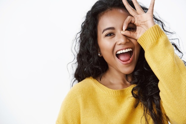 Smiling woman with curly hair playfully gesturing around her bright smile, showcasing confidence and joy.
